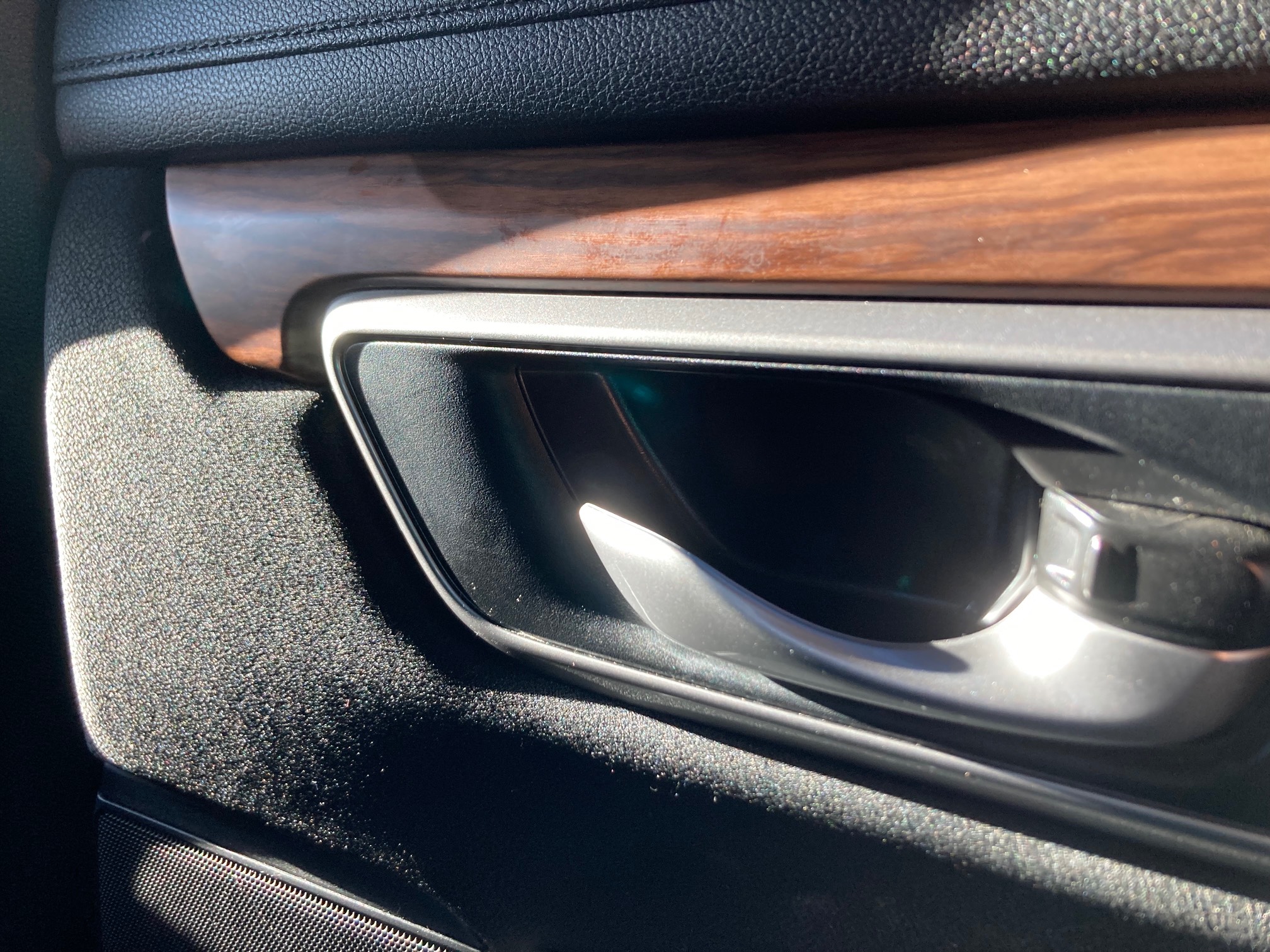 Inside of car door with handle and a slat of fake wood paneling above it