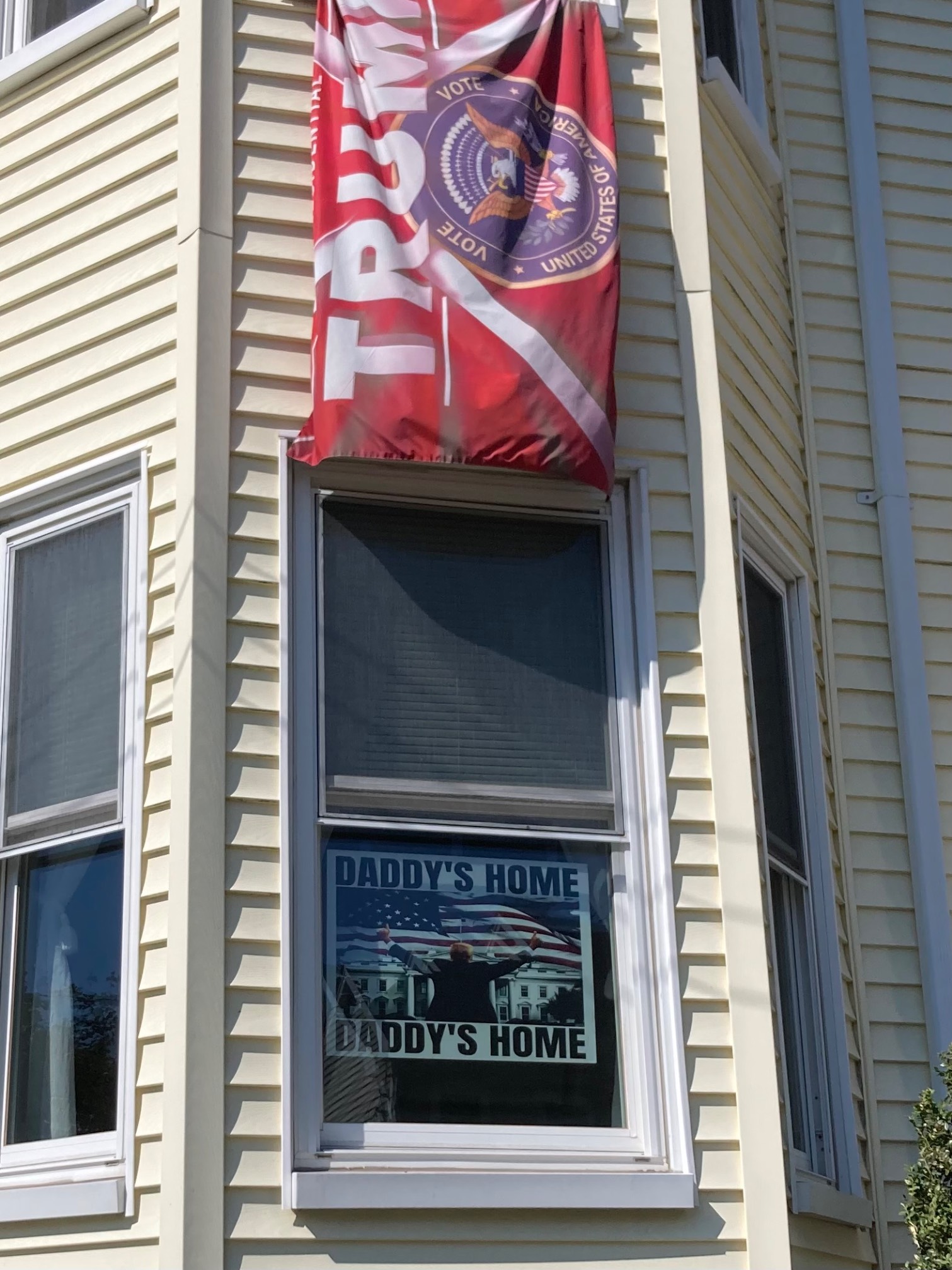 Trump banner and window with a sign showing trump with the caption “Daddy’s home”