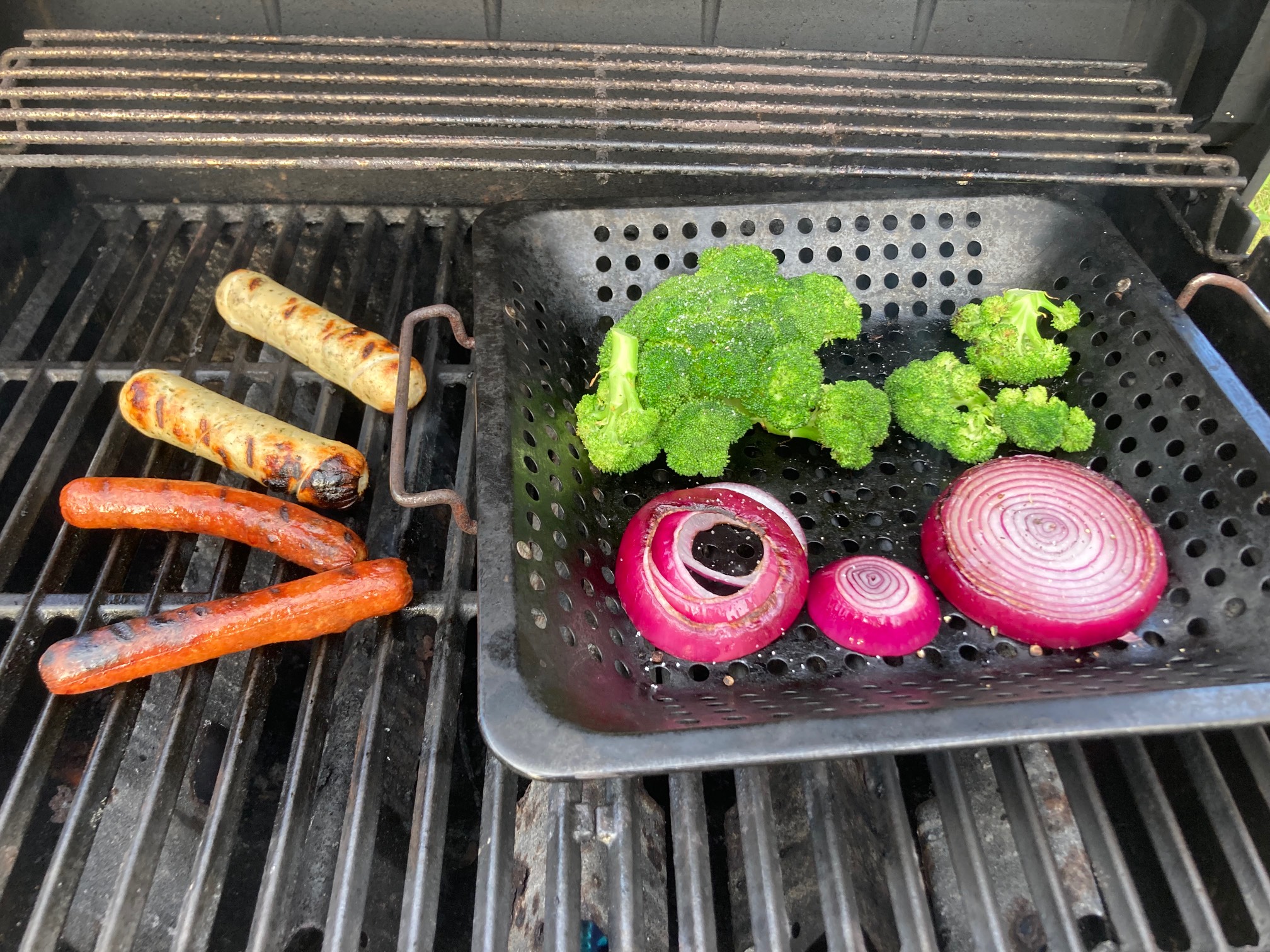 Hot dogs, broccoli, onion, and sausage on grill