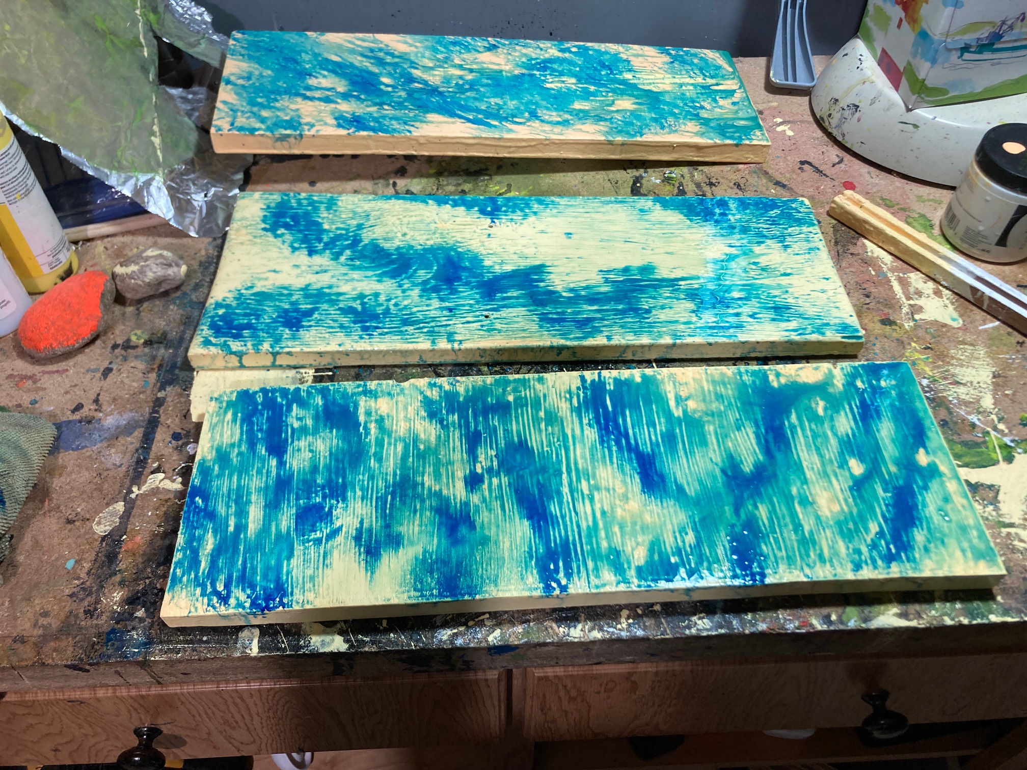 Three boards with yellow paint and watery blue paint on that.
