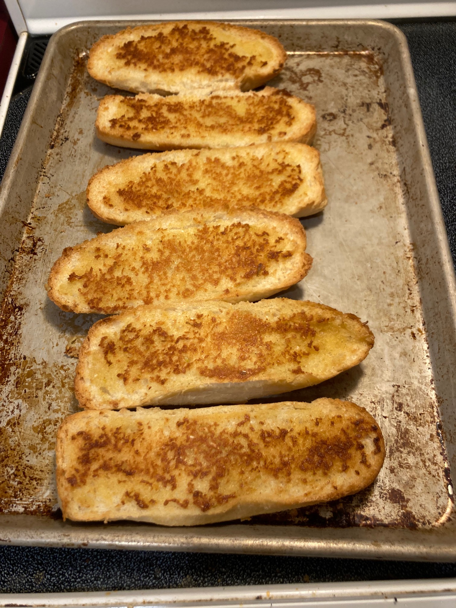 Six pill-shaped slices of garlic bread that are yellow and brown