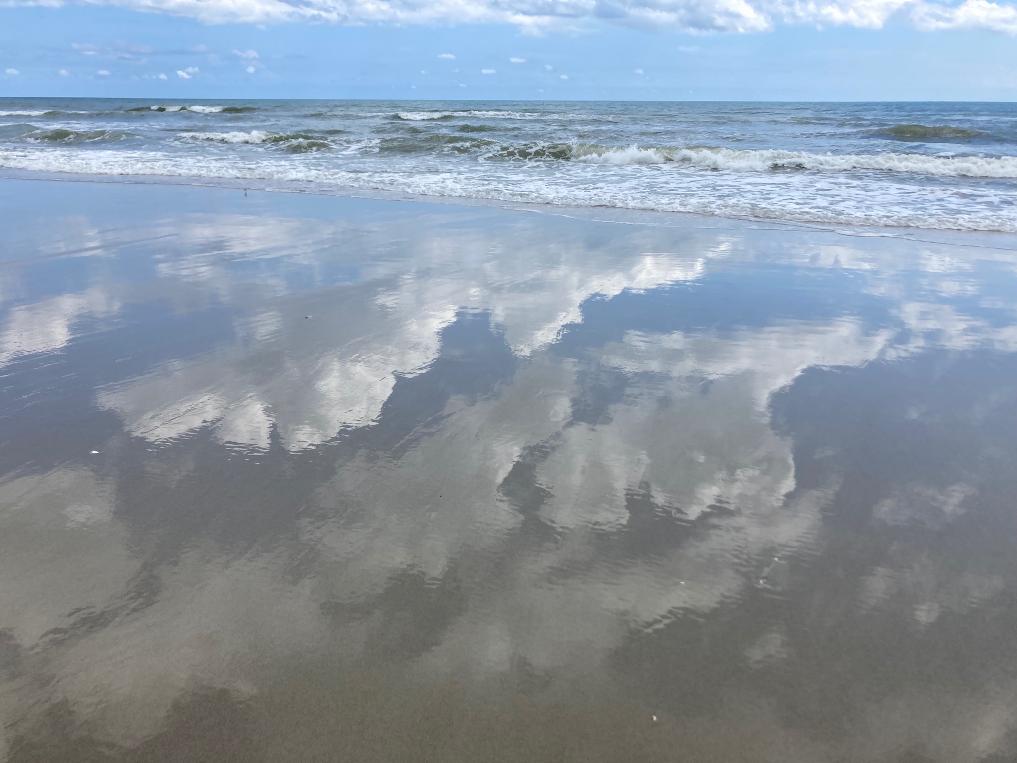 Clouds reflected in layer of water over sand