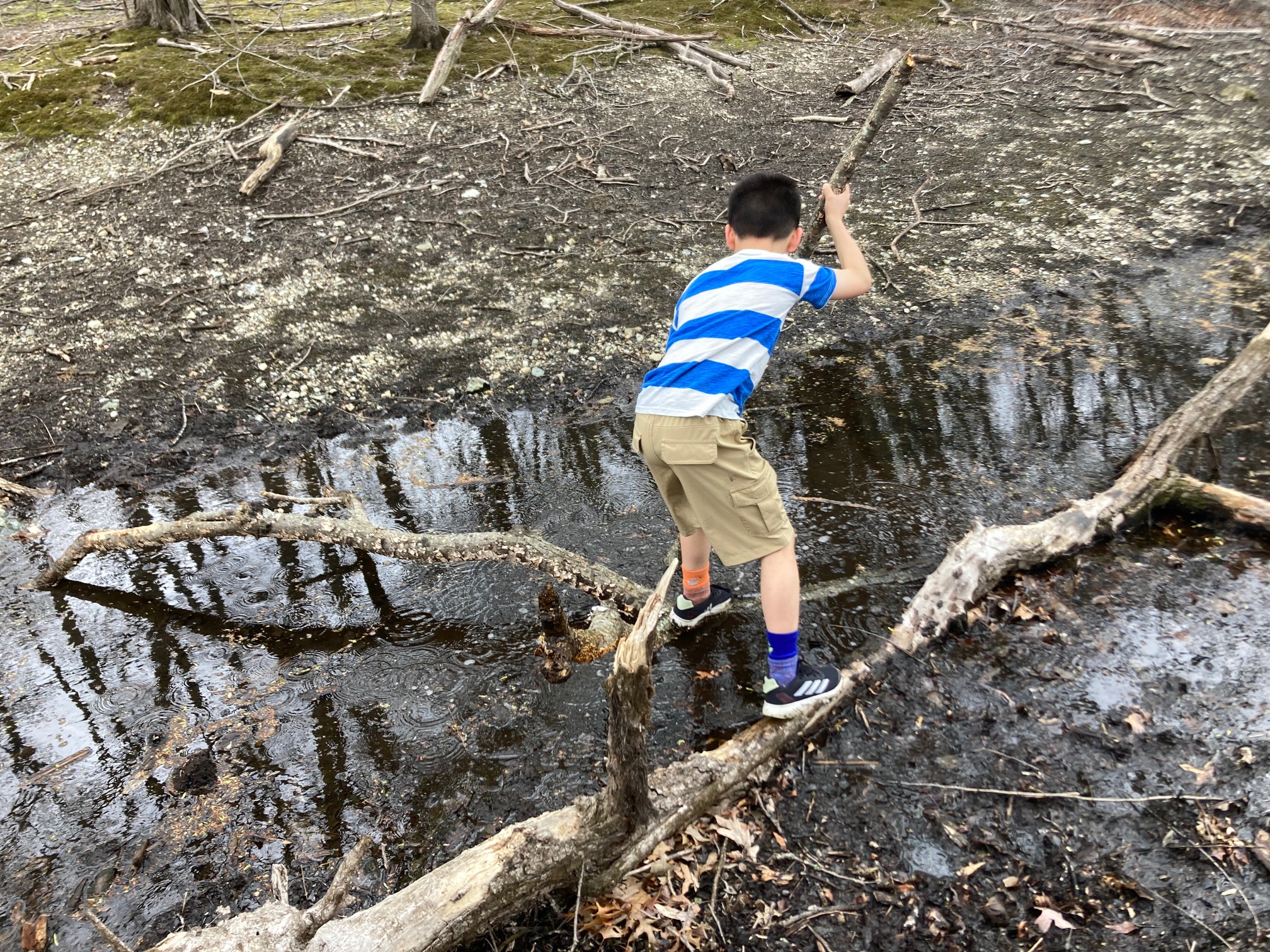 Kid walking on sticks to cross stream 