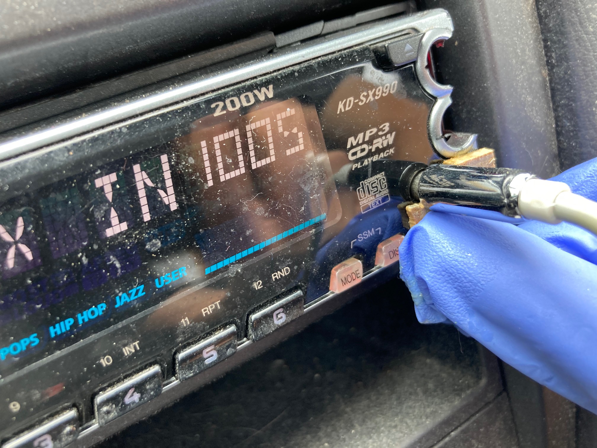 Car stereo with two small bits of wood held under the aux port by gloved hand